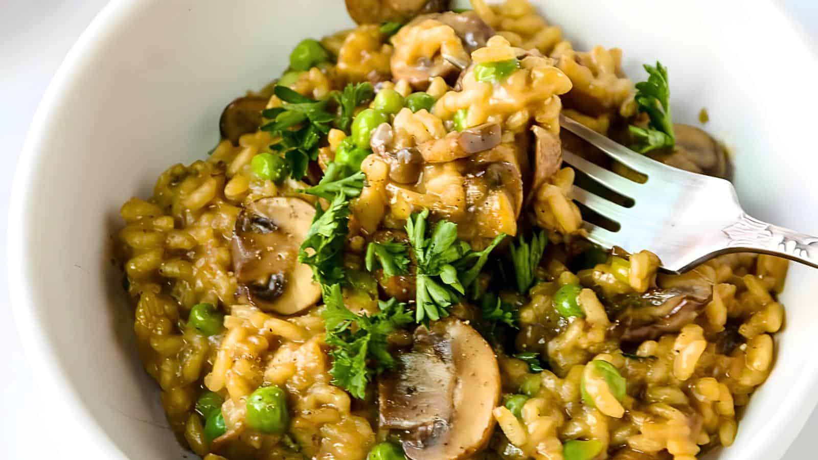 A bowl of mushroom risotto with peas, garnished with chopped parsley and a fork inserted into the risotto.