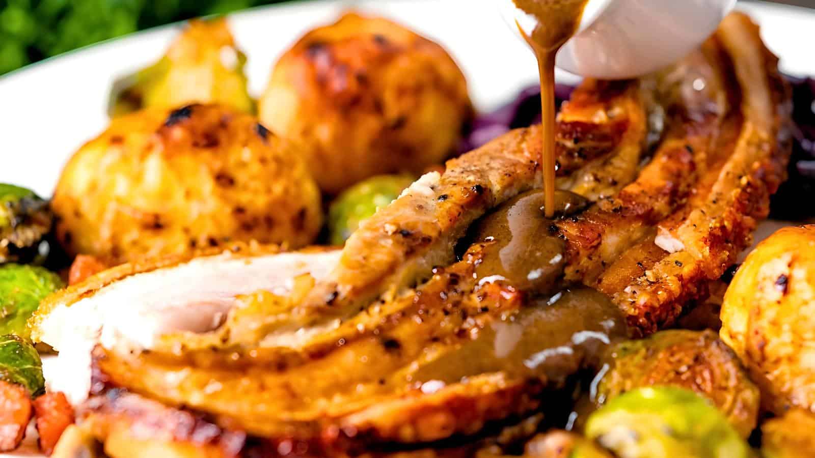 Roasted meat drizzled with brown gravy, surrounded by roasted potatoes and vegetables.