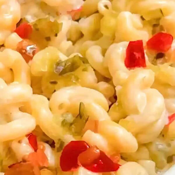Close-up of macaroni and cheese in a white dish, topped with diced red and green peppers.