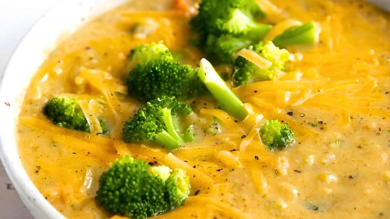 A bowl of creamy broccoli cheddar soup topped with grated cheese and a sprinkle of black pepper. Visible chunks of broccoli and melted cheese.