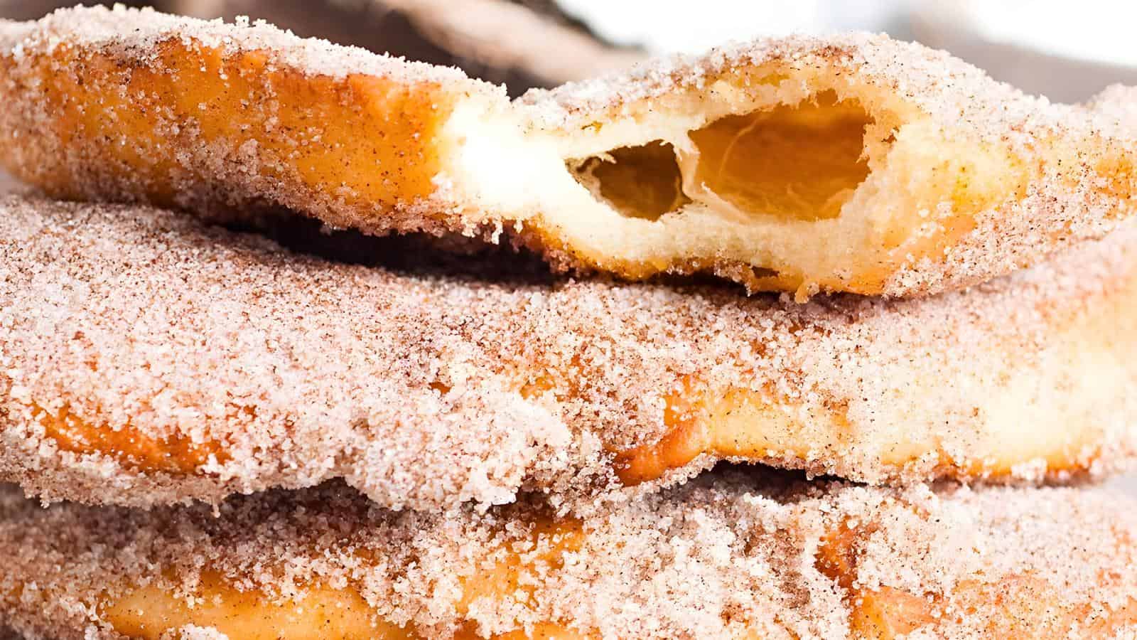 Close-up of sugar-coated fried beaver tail one with a bite taken out, revealing a hollow inside.