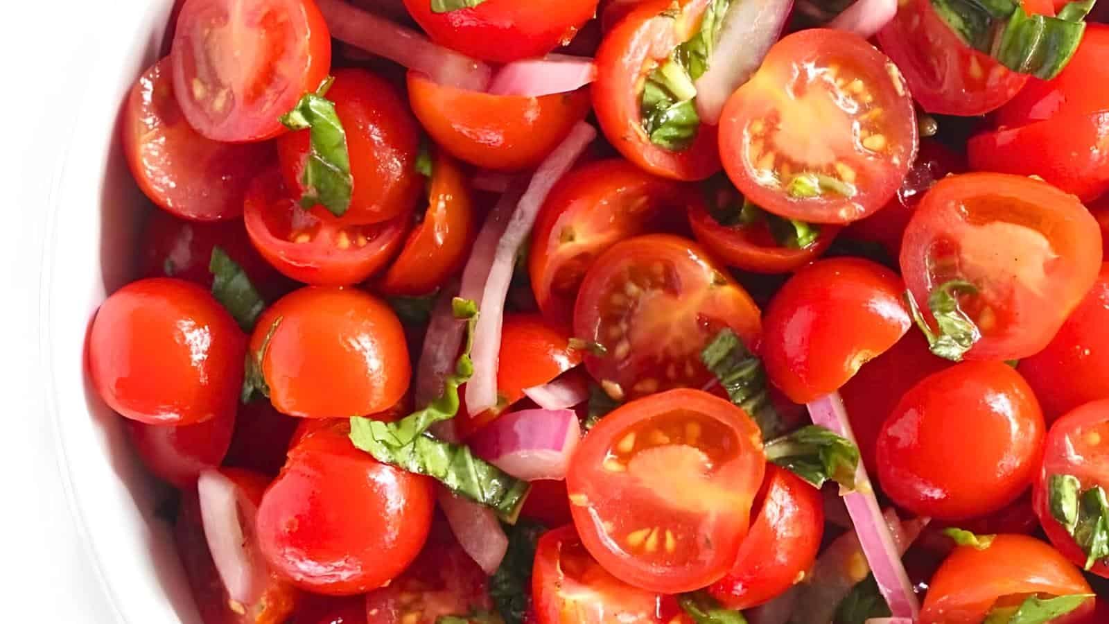 A close-up view of cherry tomatoes, sliced red onions, and chopped basil leaves.