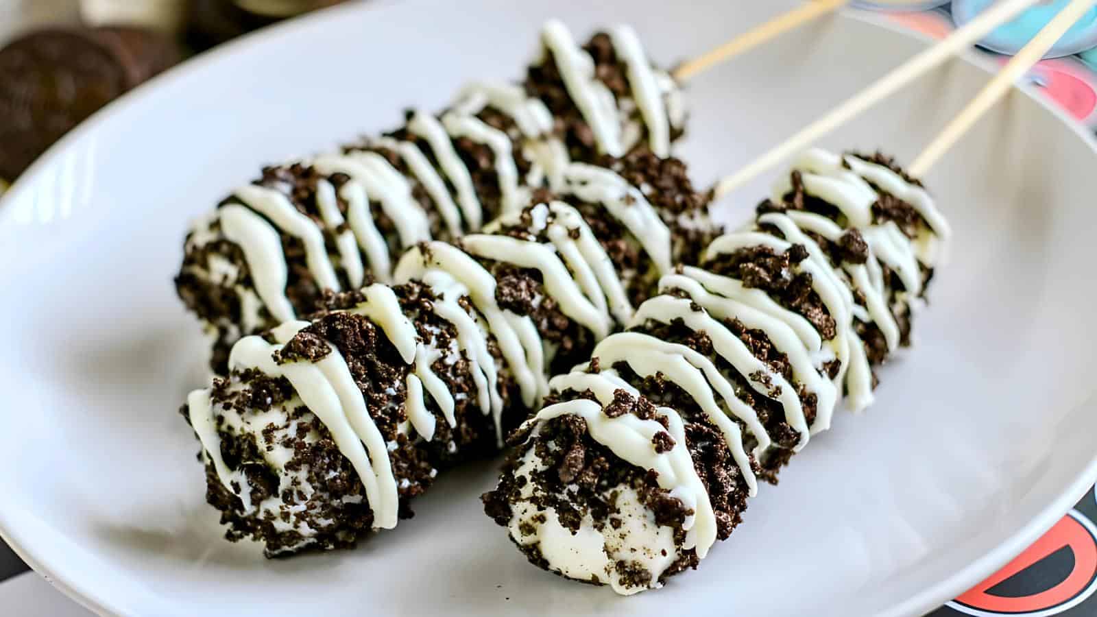 Three marshmallow pops with crushed cookies and a white drizzle.