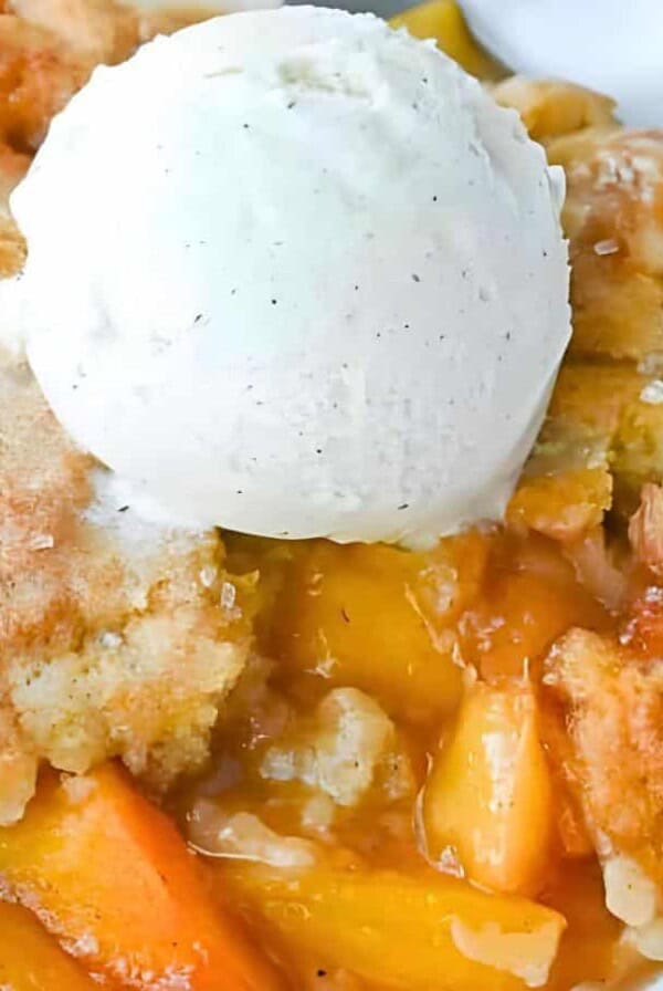 A peach cobbler topped with a scoop of vanilla ice cream, served with a spoon.