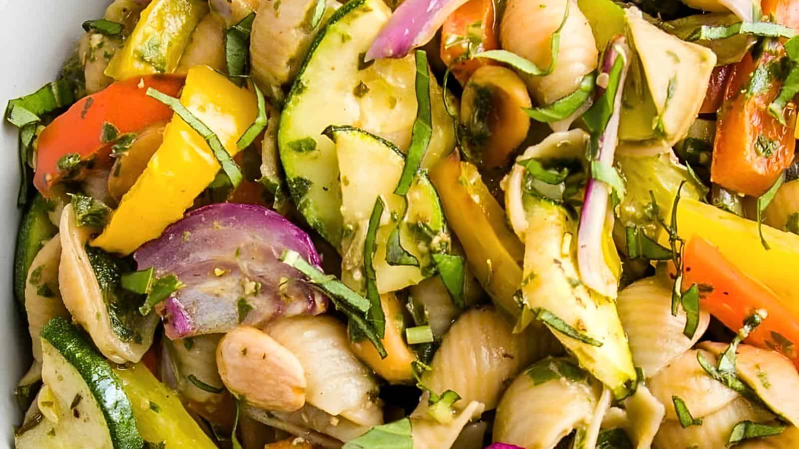 Colorful pasta salad with bell peppers, onions, zucchini, herbs, and pasta shells.