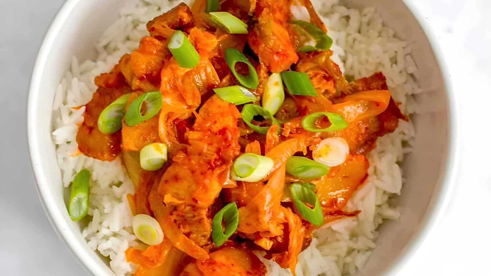 A bowl of white rice topped with chunks of meat, onions, and sliced green onions.