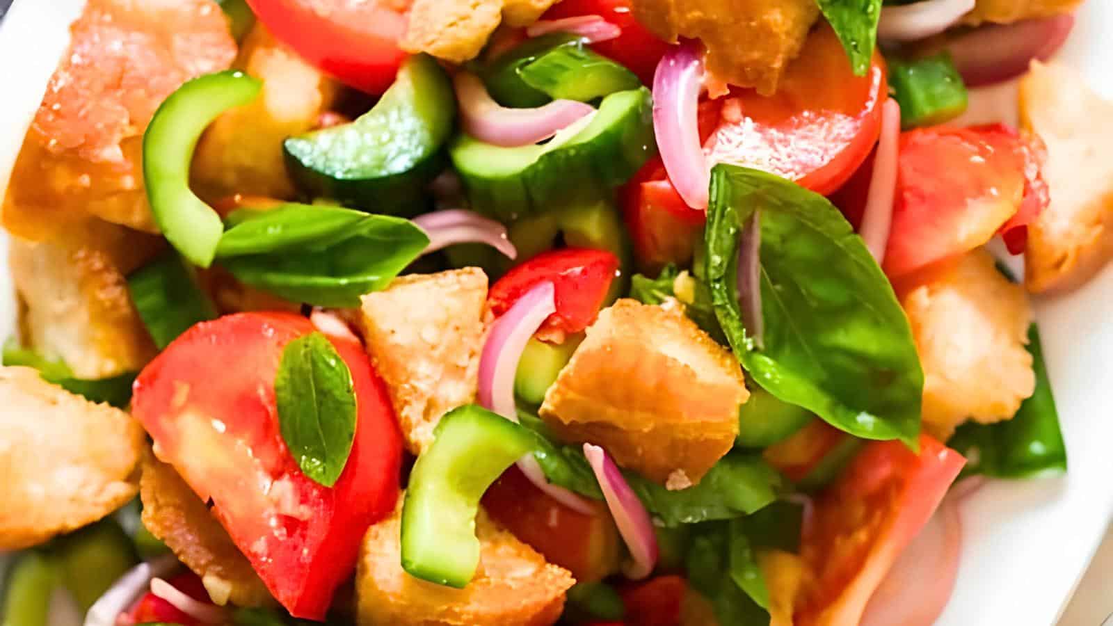 A bowl containing tomatoes, cucumber slices, red onions, basil leaves, and pieces of bread.