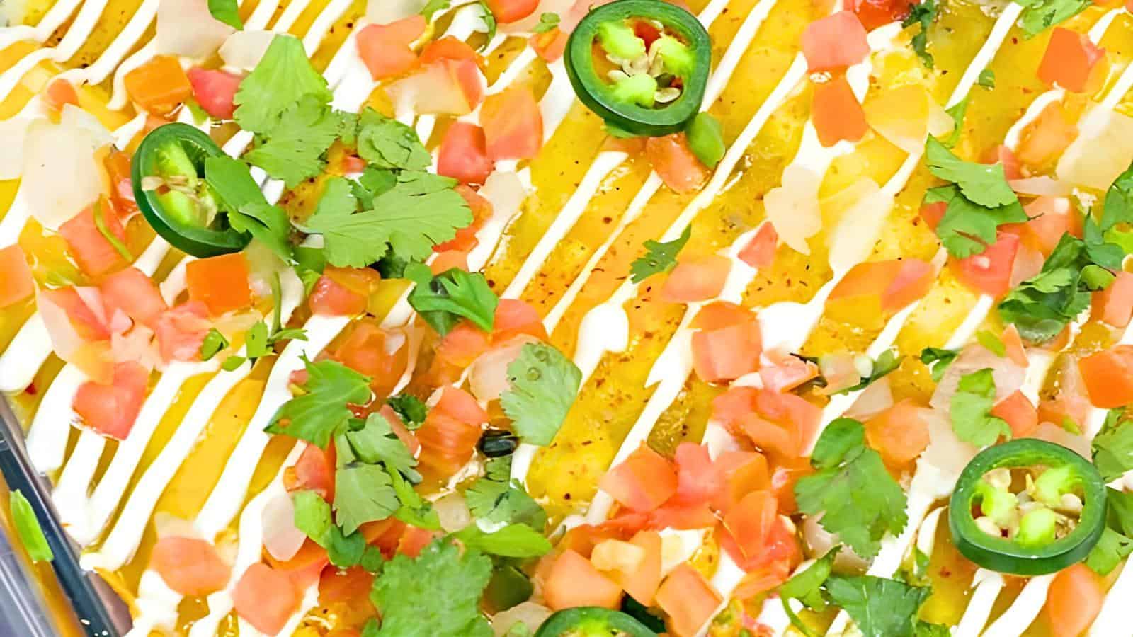 A dish topped with diced tomatoes, cilantro, jalapeño slices, and white and yellow sauce drizzles.
