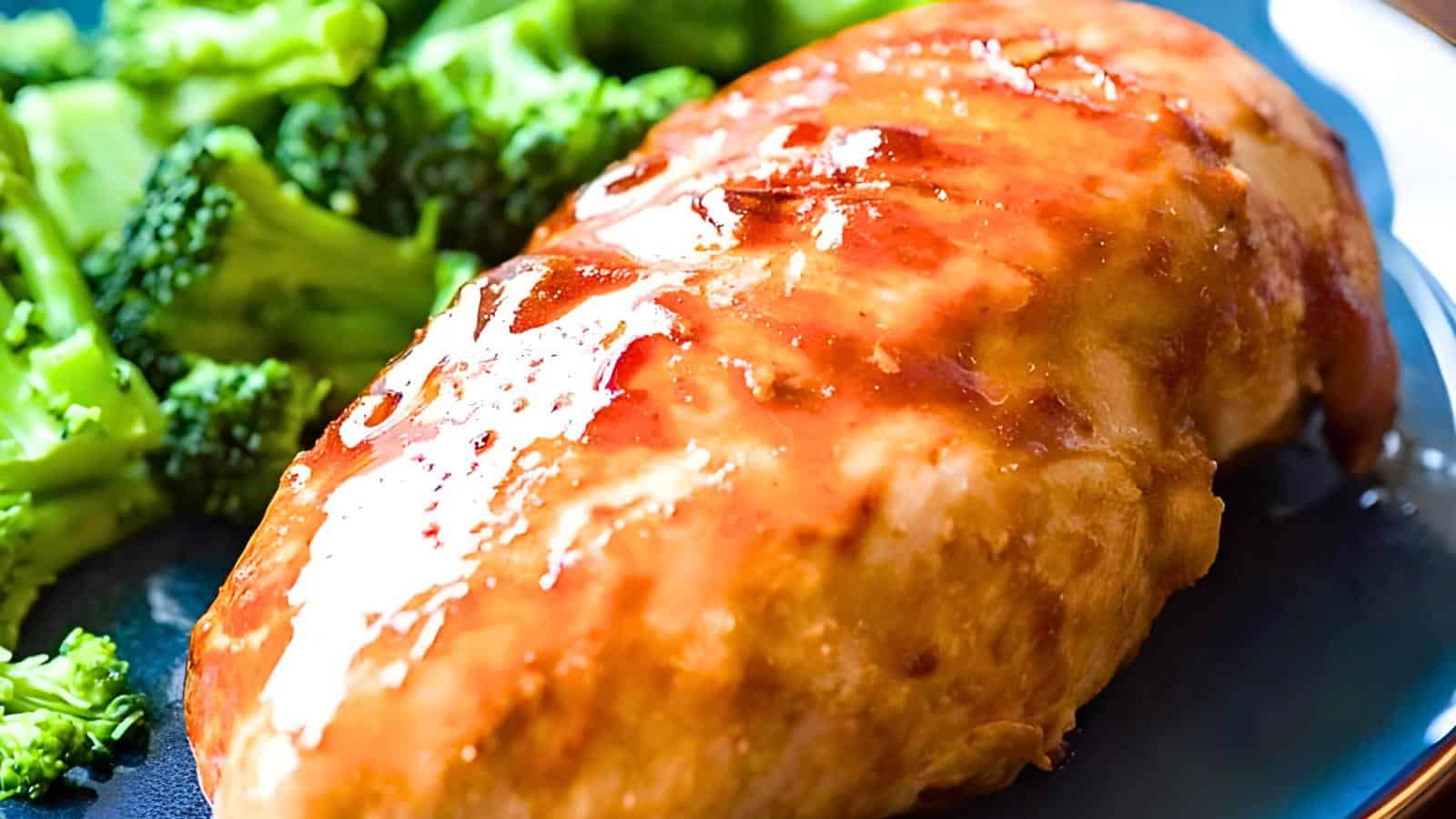 A glazed chicken breast is served on a blue plate with broccoli florets on the side. The chicken has a shiny, golden-brown finish, suggesting a flavorful sauce or marinade.