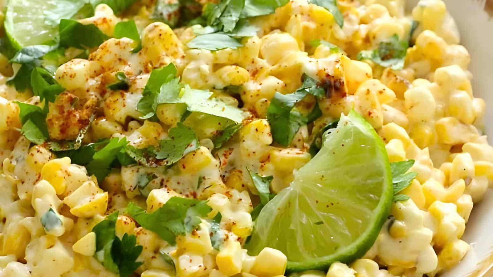 A dish of creamy corn salad garnished with chopped cilantro, a lime wedge, and sprinkled with chili powder.