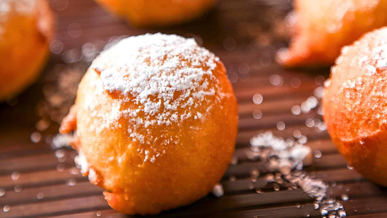 Golden brown zeppole sprinkled with powdered sugar on a wooden surface.