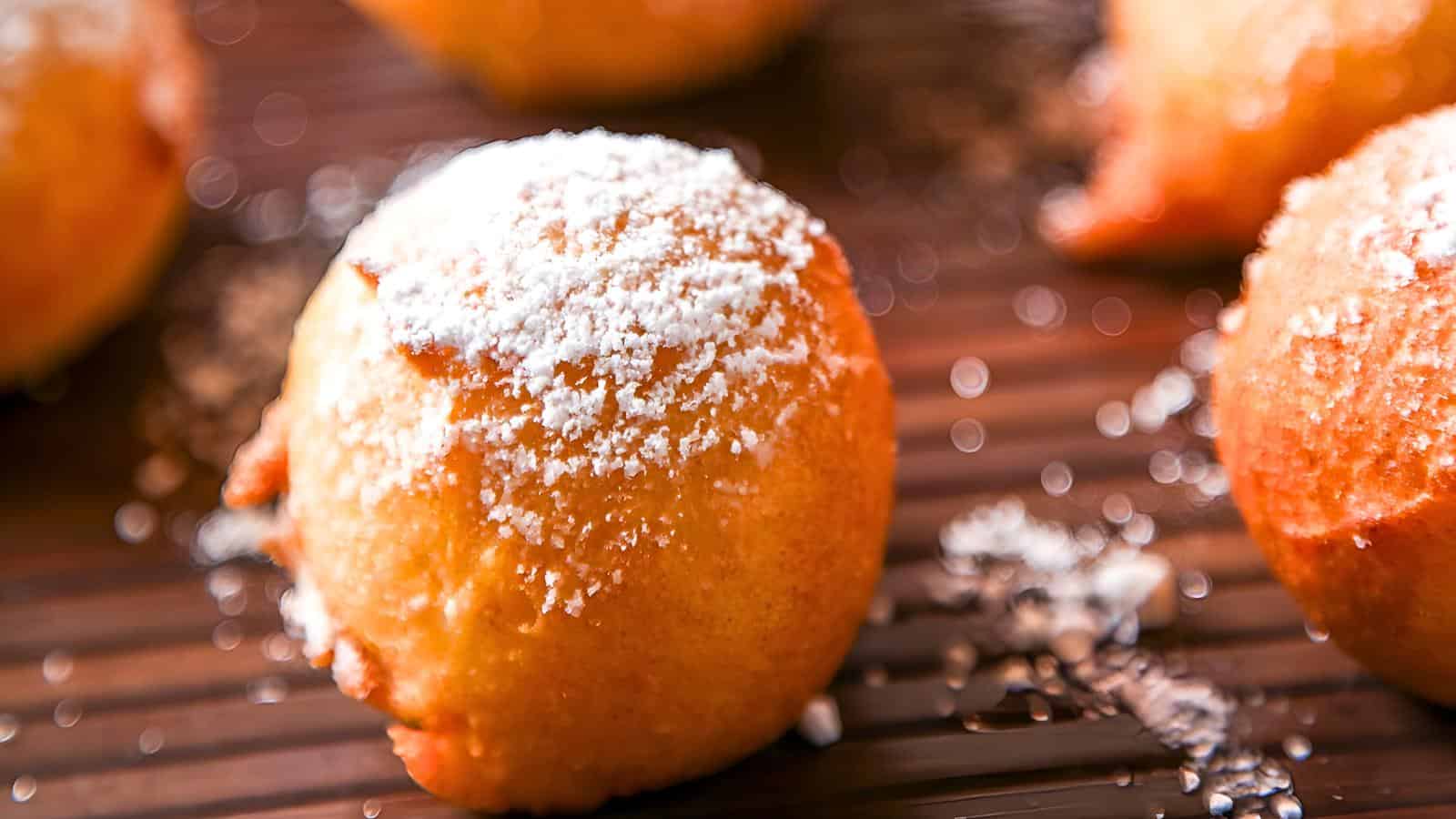 A powdered sugar-dusted zeppole on a wooden surface, with blurred zeppole in the background.