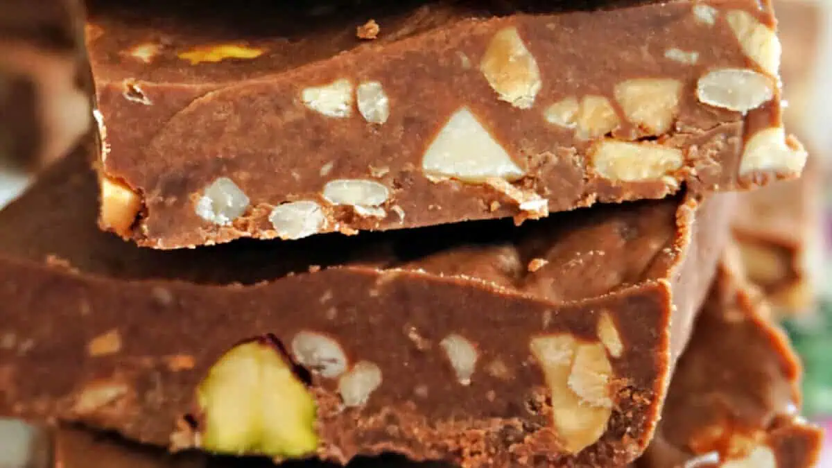Close-up of a stack of milk chocolate bars filled with chopped nuts. The image shows the texture and assorted nuts embedded within the chocolate, highlighting a rich, creamy composition with bits of crunchy nuts distributed throughout.