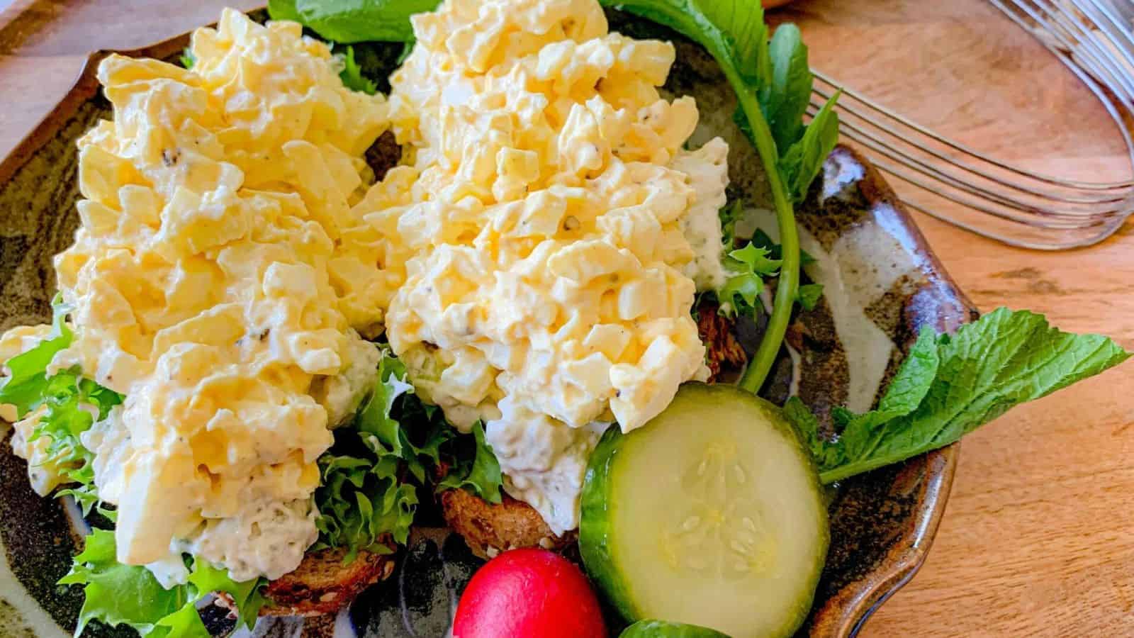 An open faced sandwich of egg salad on a plate with a radish.