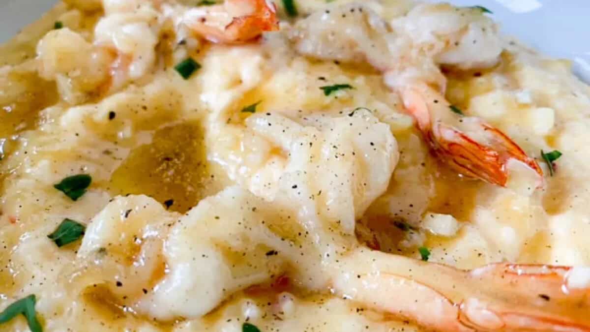 Close-up of shrimp and grits topped with brown gravy, chopped herbs, and black pepper.