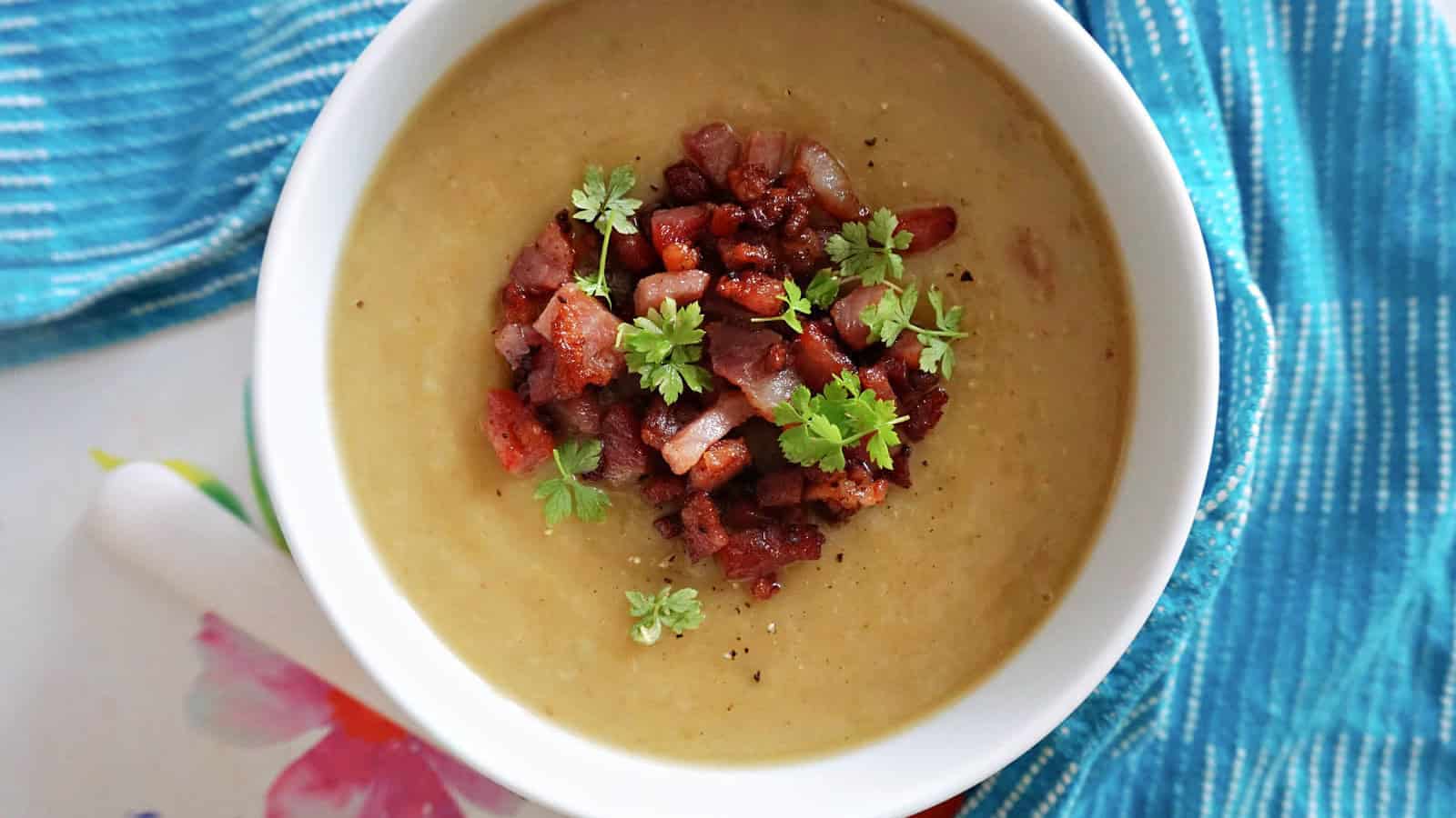 A portion of leek and potato soup topped with a handful of bacon bites.