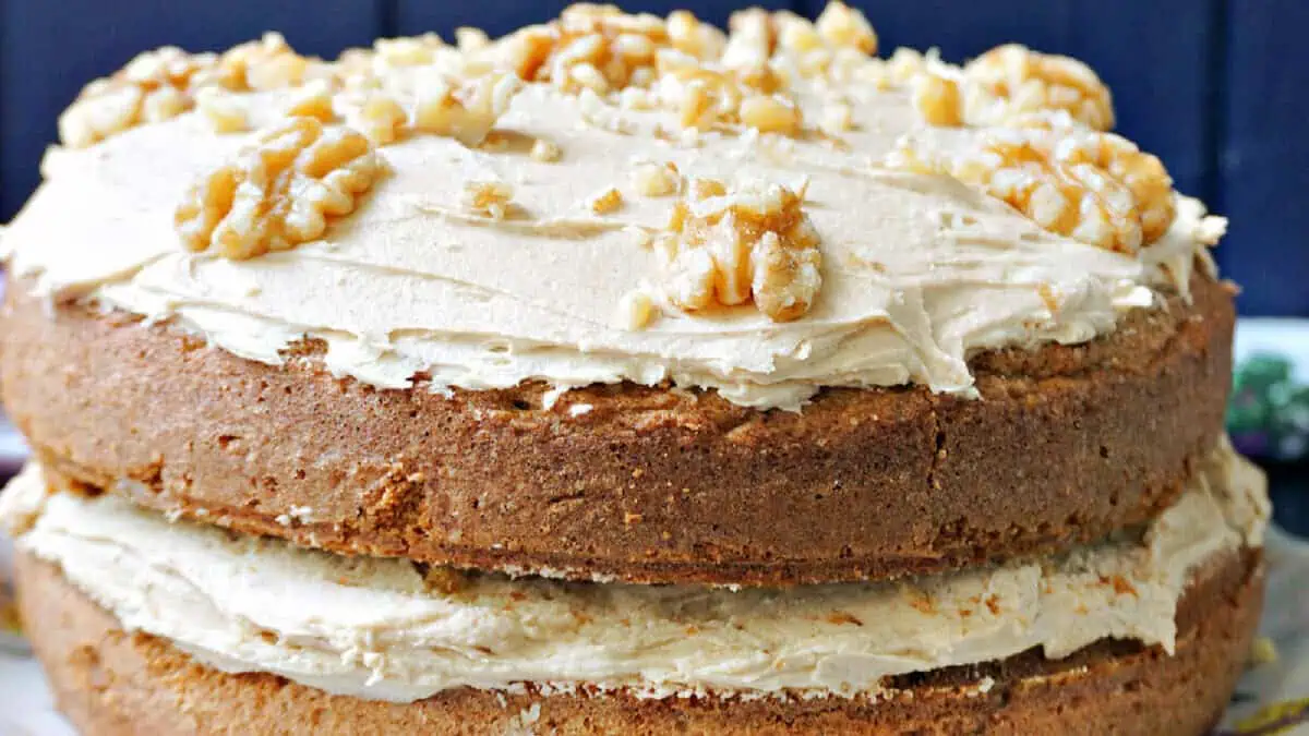 A two-layer coffee and walnut cake. Each layer is separated by a thick, creamy coffee frosting, which also covers the top of the cake. Decoratively placed walnut halves are evenly spread over the top layer of frosting.