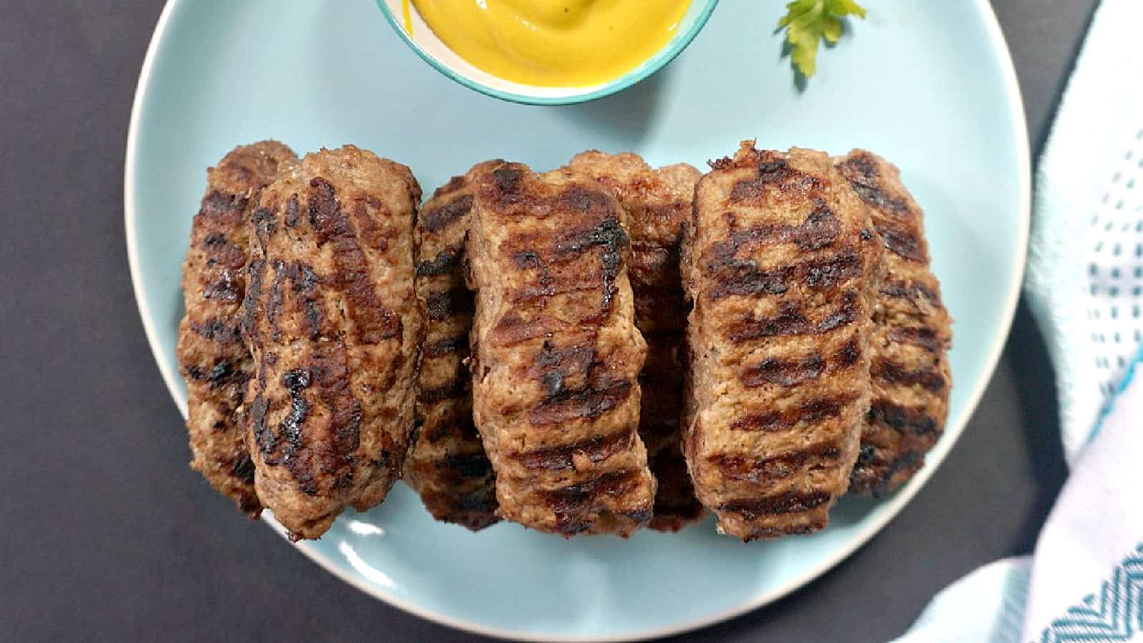 Mici on a blue plate with a ramekin of mustard.