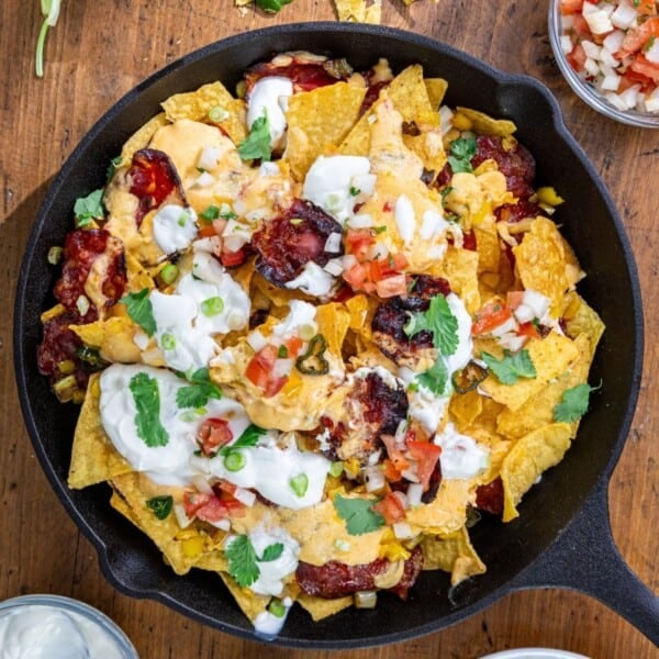 Pimento cheese nachos in a cast iron skillet, topped with melted cheese, sour cream, salsa, cilantro, and green onions.