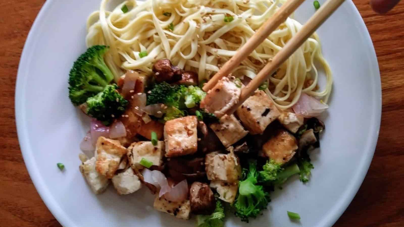 sesame ginger tofu with broccoli and noodles on plate with chopsticks.