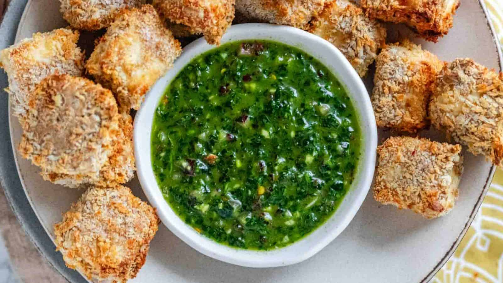 A bowl with green herby sauce surrounded by breaded cubes.