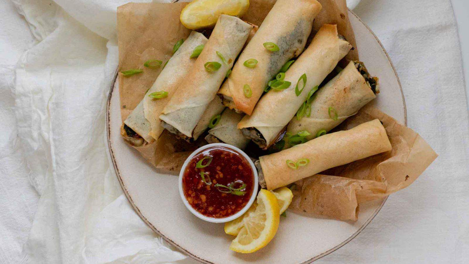 Rolled baked pastries on plate with a small bowl of sauce.