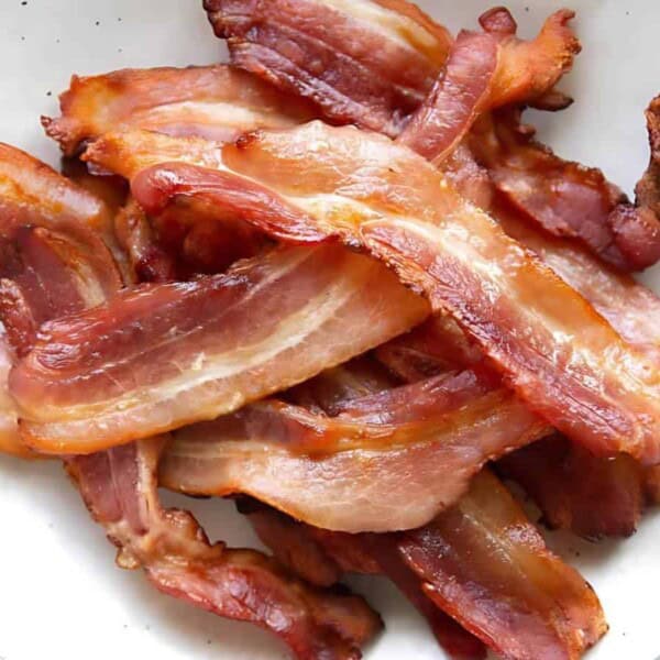 A white plate with several strips of crispy cooked bacon stacked.