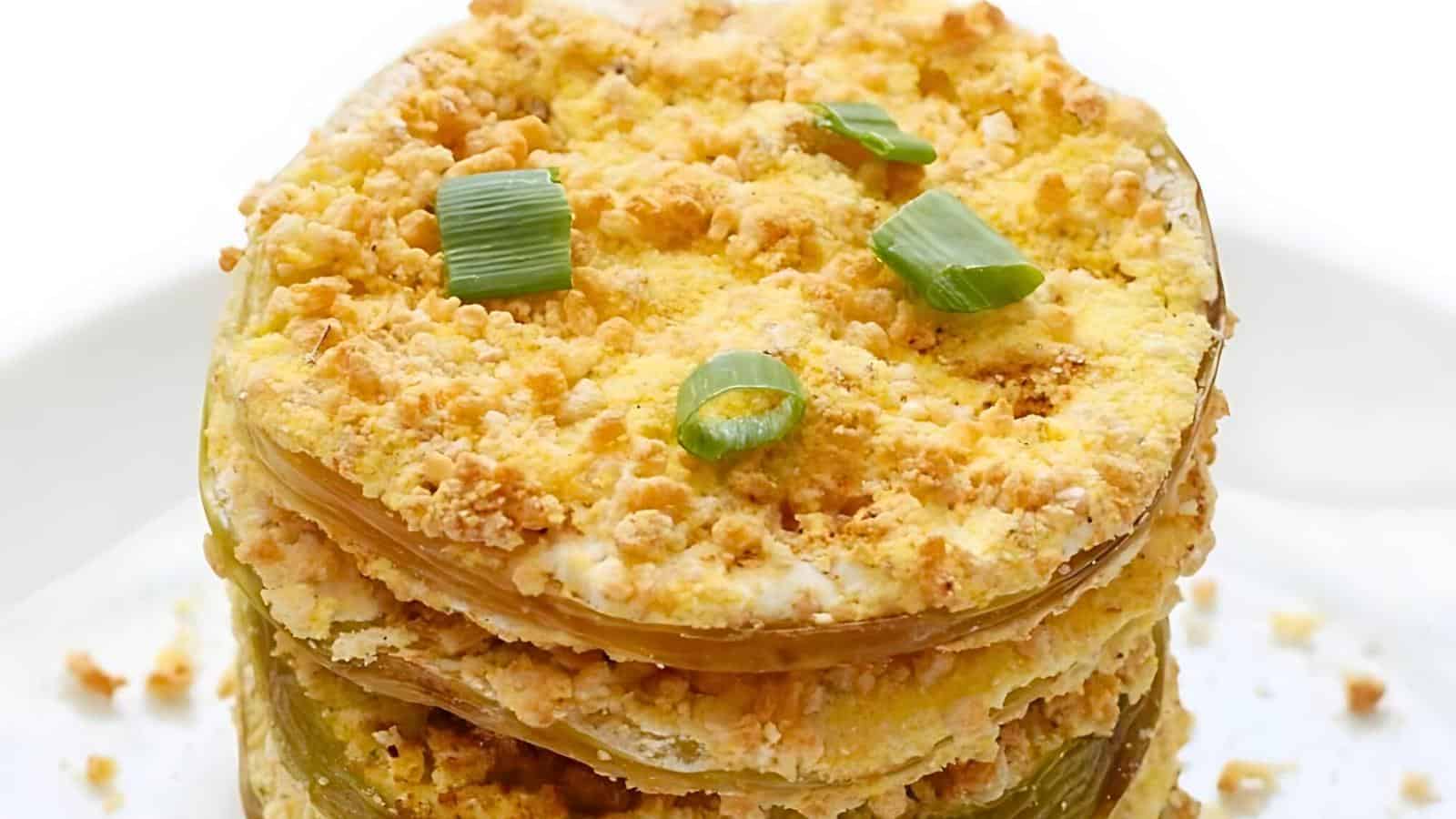 A stack of baked green tomato slices with a crunchy breadcrumb crust, garnished with chopped green onions on a white plate.