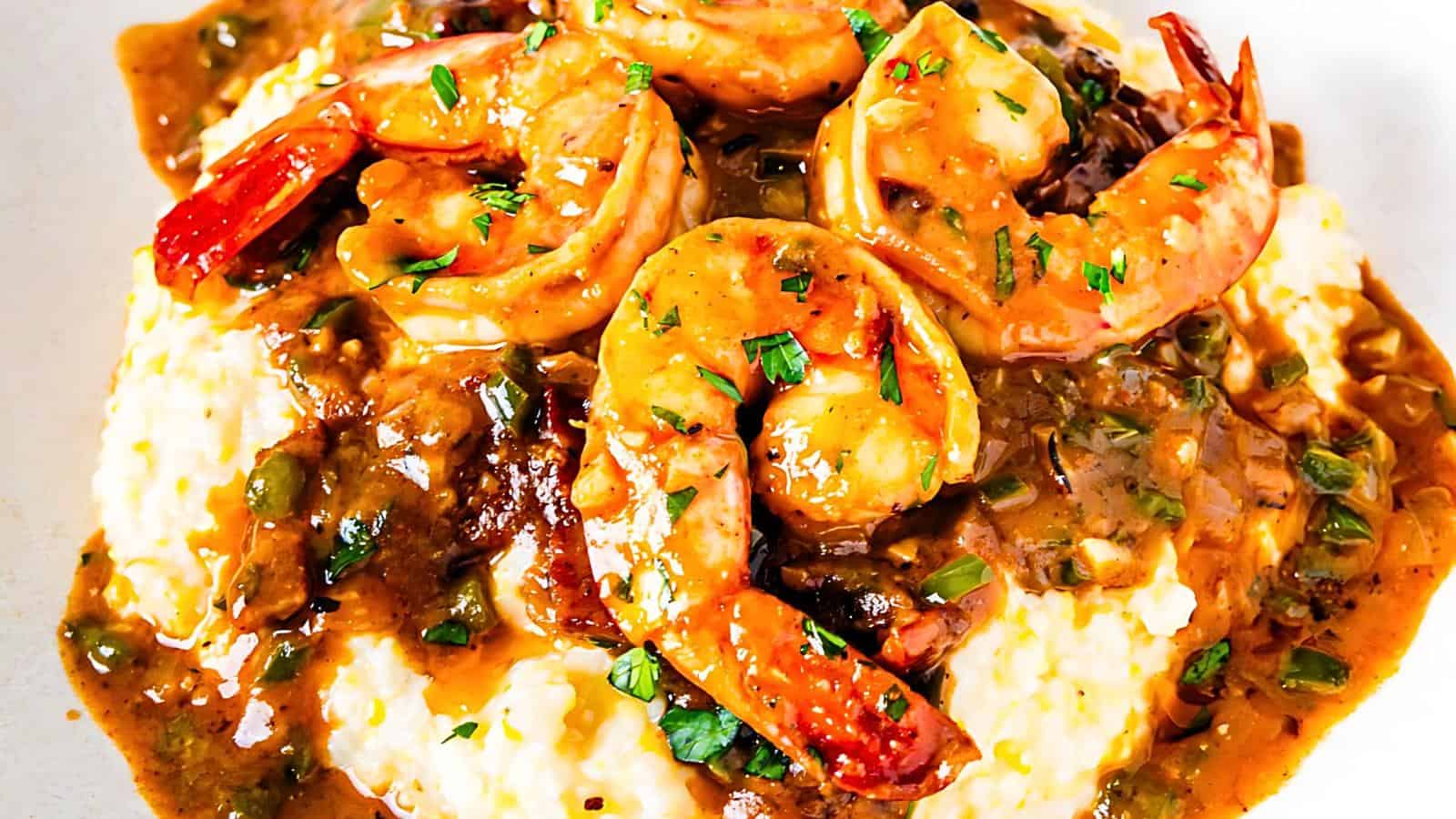 A plate of creamy grits topped with shrimp in a savory brown sauce, garnished with chopped herbs.