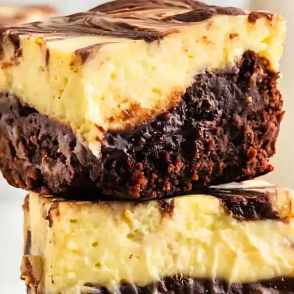 Two stacked marbled cheesecake brownies with layers of chocolate brownie and creamy cheesecake swirled with chocolate.