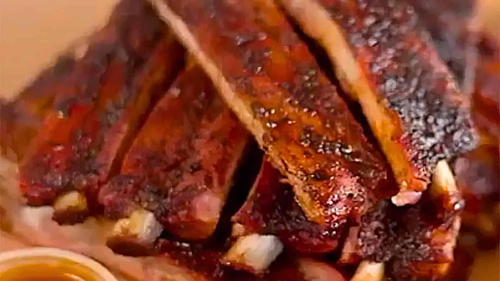 A stack of barbecued ribs with a caramelized exterior, visible seasoning, and grill marks, glazed with a sauce.