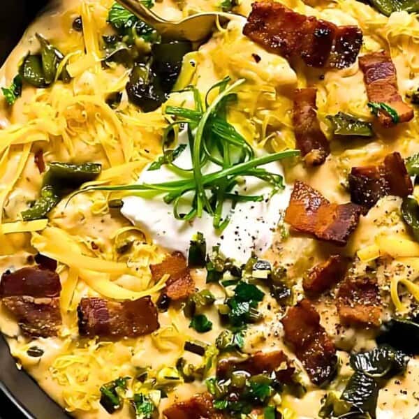 A soup with roasted green chiles, crispy bacon, melted cheese, a dollop of sour cream, and garnished with sliced green onions.