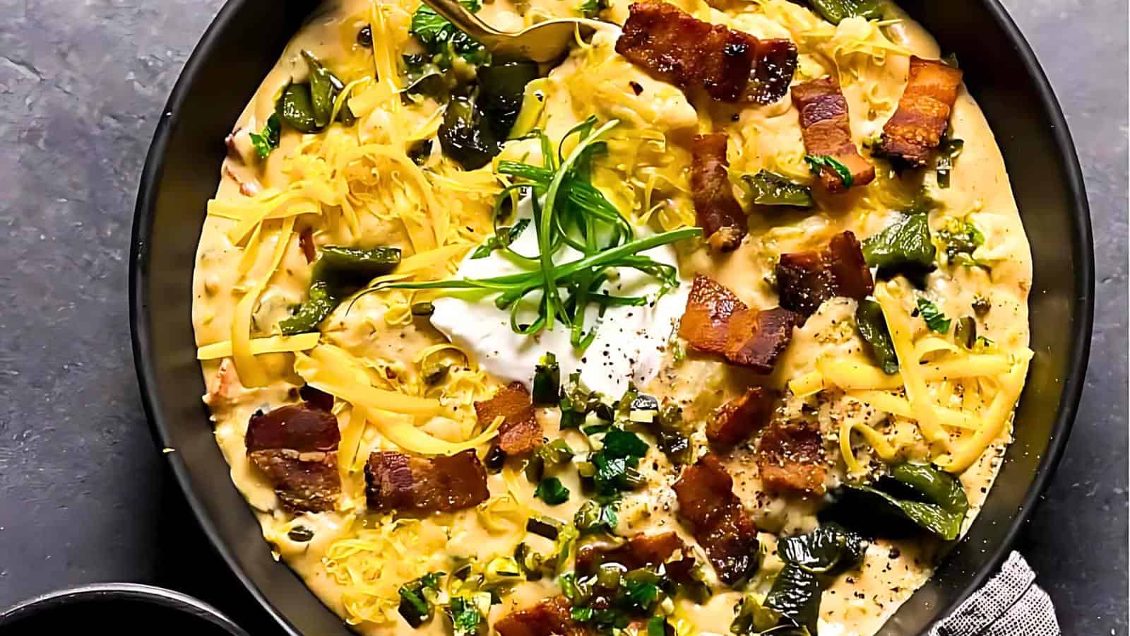 A soup with roasted green chiles, crispy bacon, melted cheese, a dollop of sour cream, and garnished with sliced green onions.