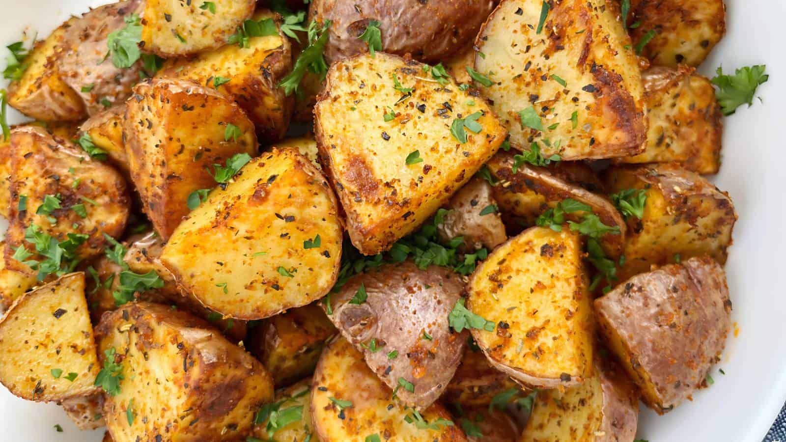 Roasted potato wedges seasoned with herbs and spices, garnished with chopped parsley.