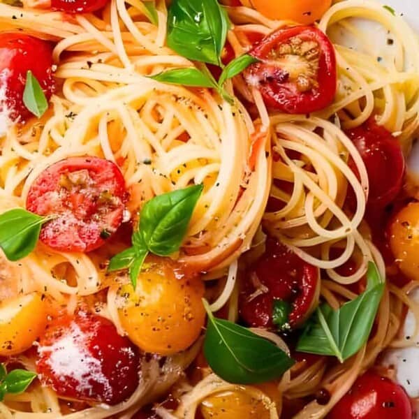 A plate of spaghetti topped with red and yellow cherry tomatoes, fresh basil leaves, grated parmesan cheese, and a sprinkling of black pepper.