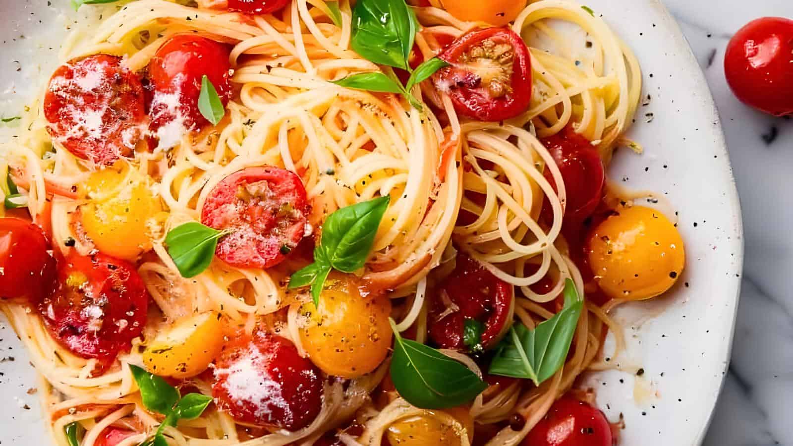 A plate of spaghetti topped with red and yellow cherry tomatoes, fresh basil leaves, grated parmesan cheese, and a sprinkling of black pepper.
