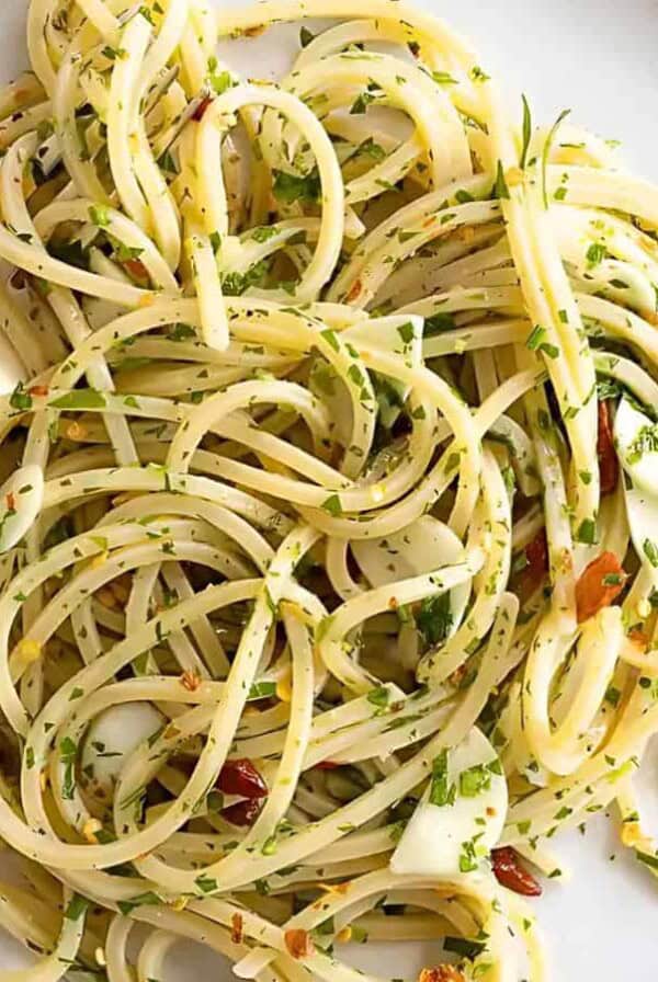 A plate of spaghetti aglio e olio topped with chopped parsley and garlic slices, with a fork resting on the side.