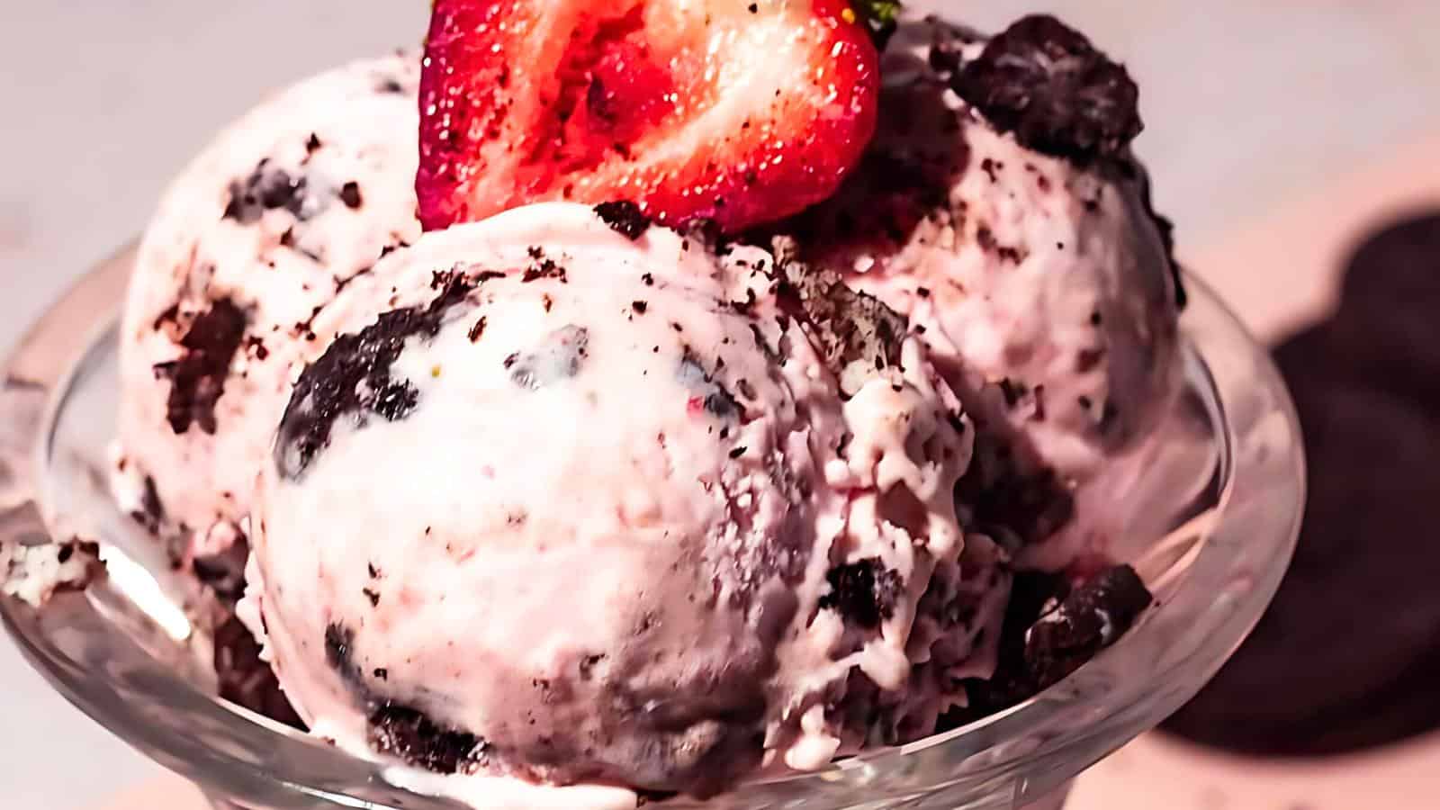 A glass bowl filled with scoops of strawberry ice cream mixed with chocolate cookie pieces, topped with a fresh strawberry slice.