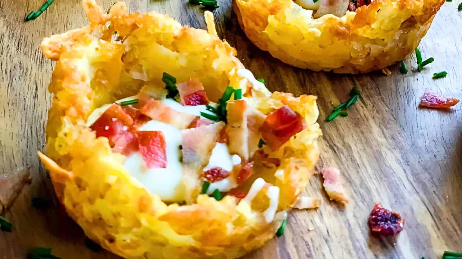 Close-up of crispy hash brown cups filled with diced bacon, melted cheese, and chopped herbs on a wooden surface.