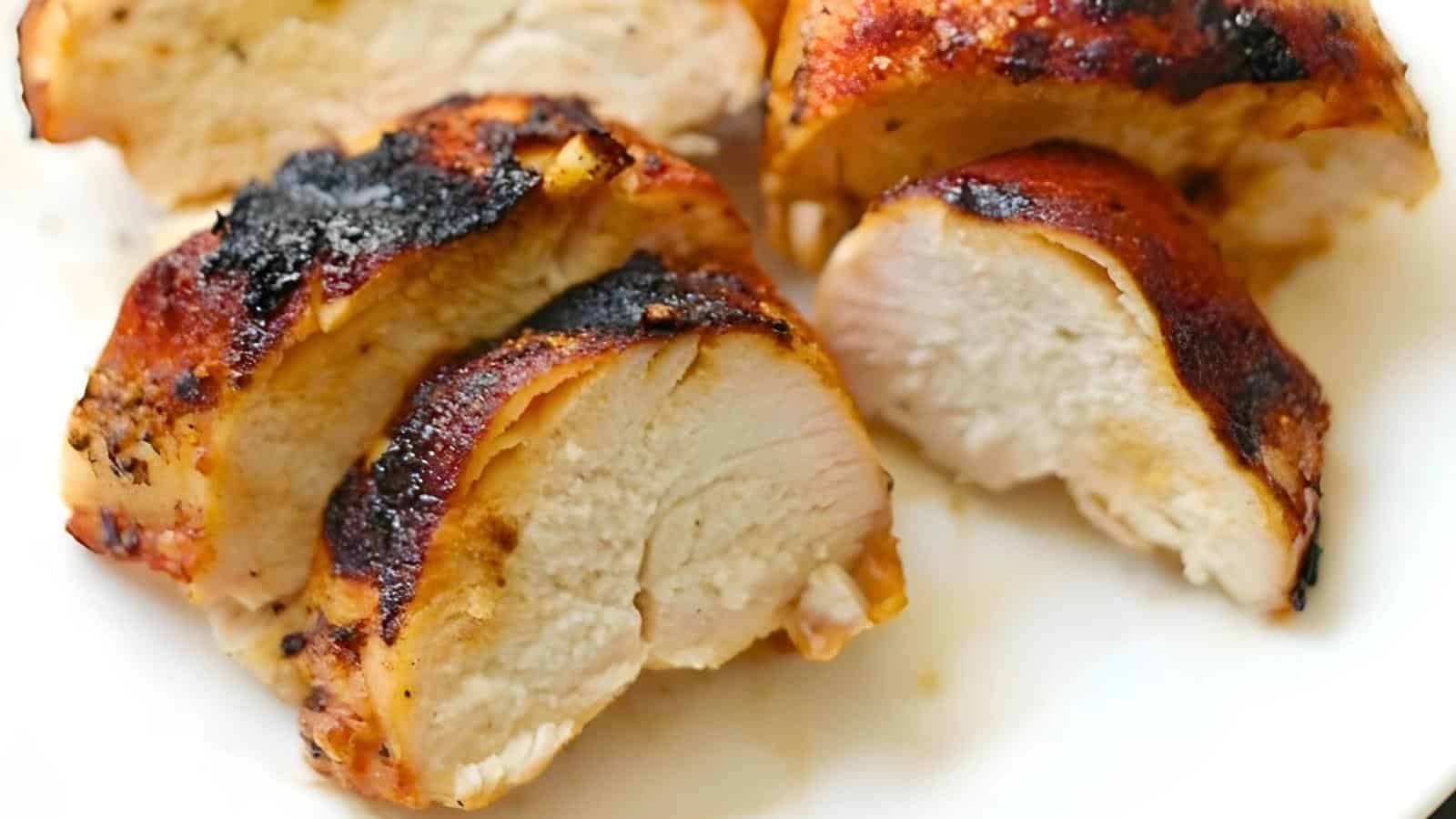 Sliced grilled chicken with a browned, crispy exterior on a white surface.