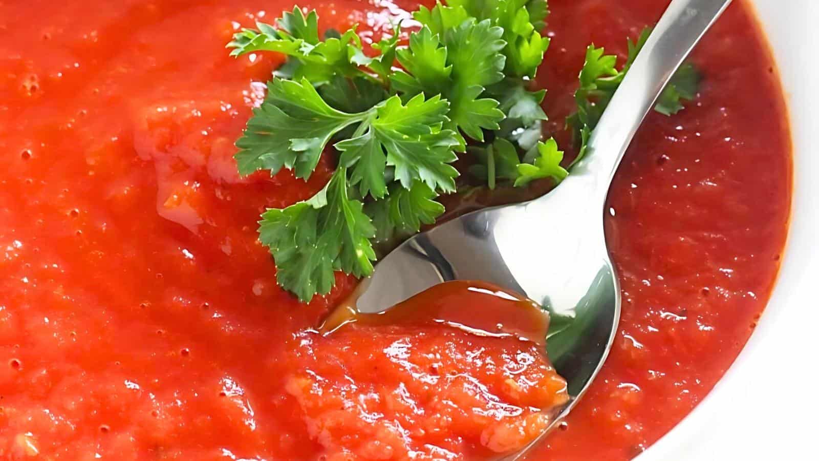 A bowl of tomato soup garnished with fresh parsley and a spoon partially submerged in the soup.