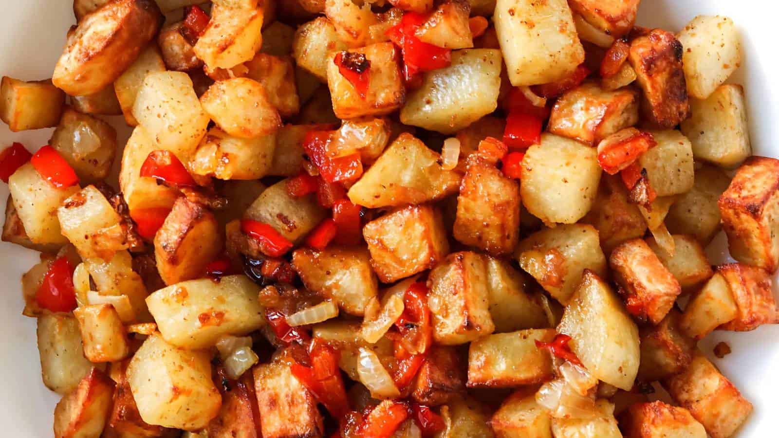 Roasted potatoes mixed with chopped red bell peppers and onions, displaying a golden-brown and caramelized texture.