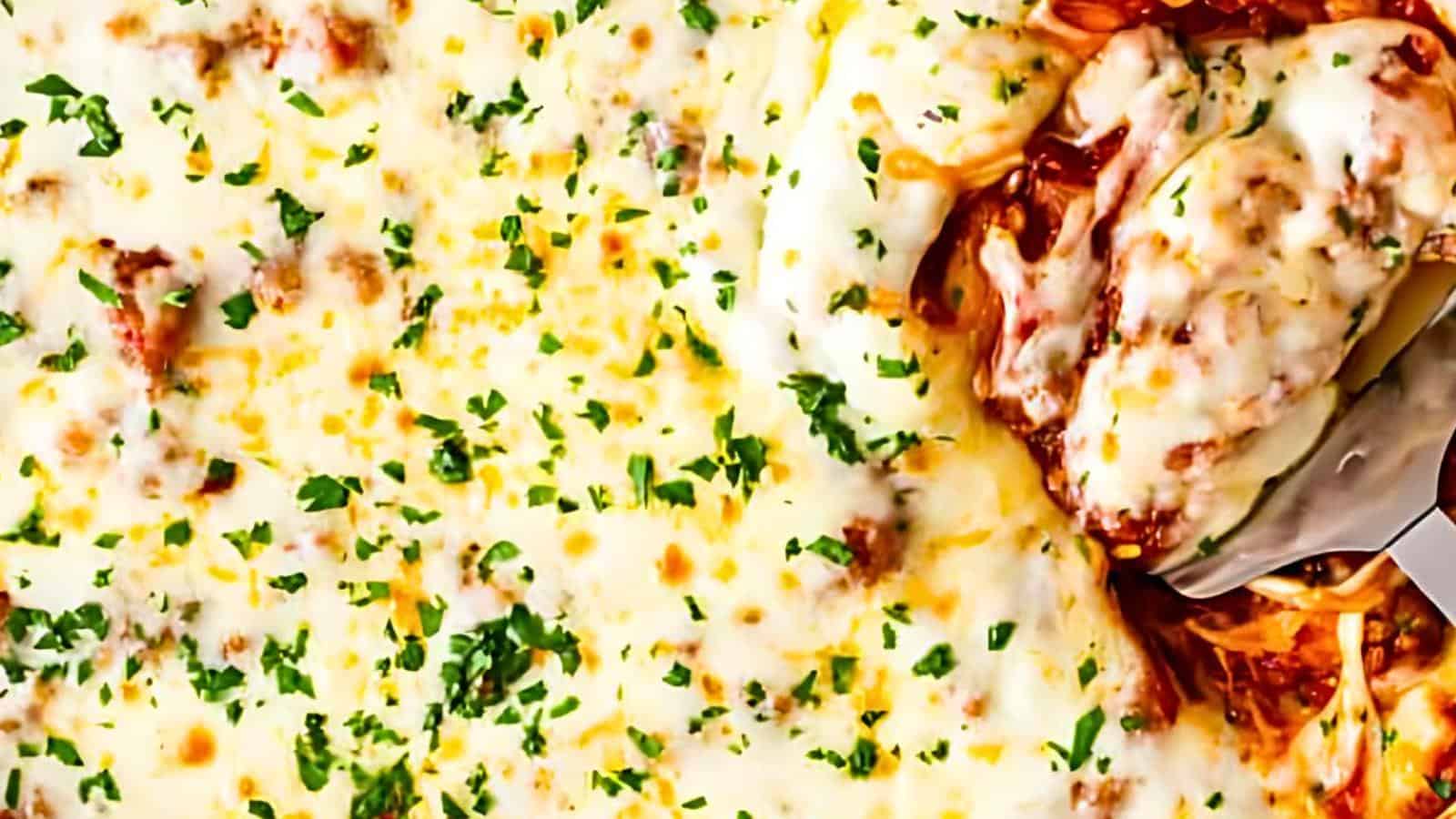Baked spaghetti topped with melted cheese and garnished with chopped parsley. A serving spatula lifting a portion, revealing spaghetti strands mixed with sauce.