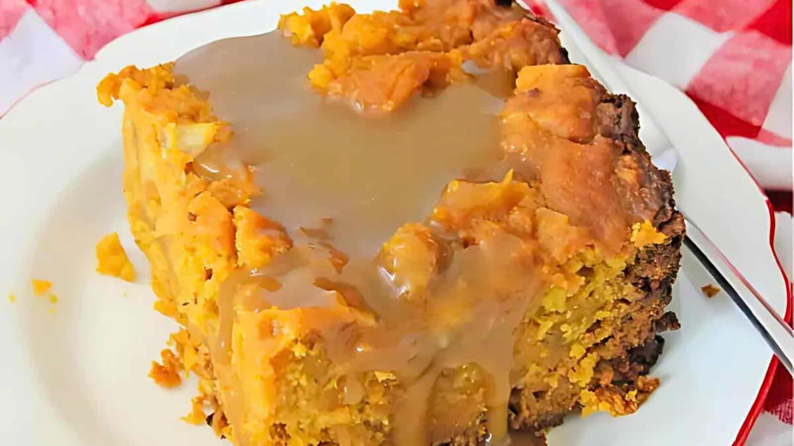 A piece of gooey dessert covered with caramel sauce on a white plate with a red and white checkered cloth in the background.