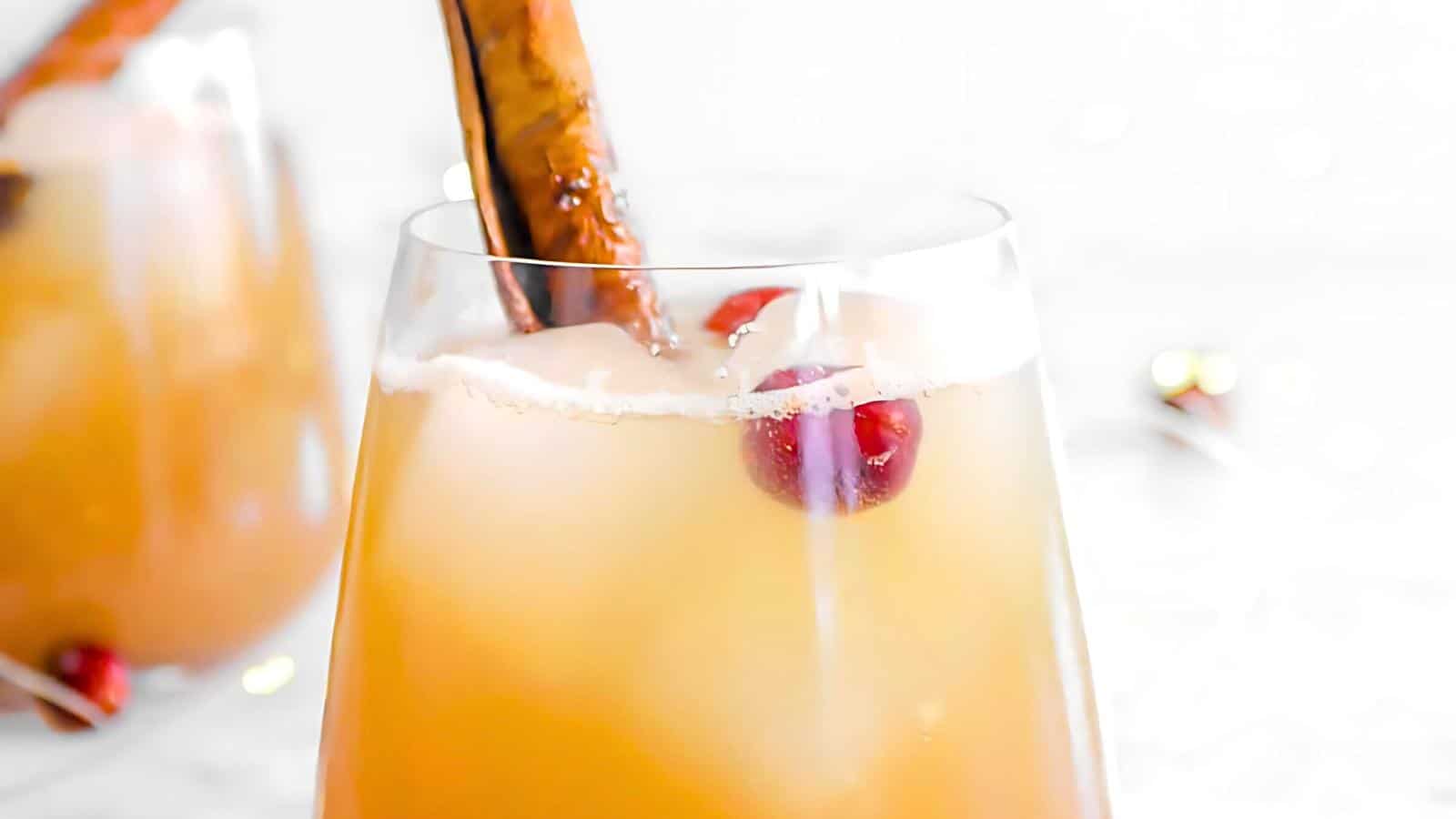 A glass filled with a light orange beverage, garnished with cranberries and a cinnamon stick.