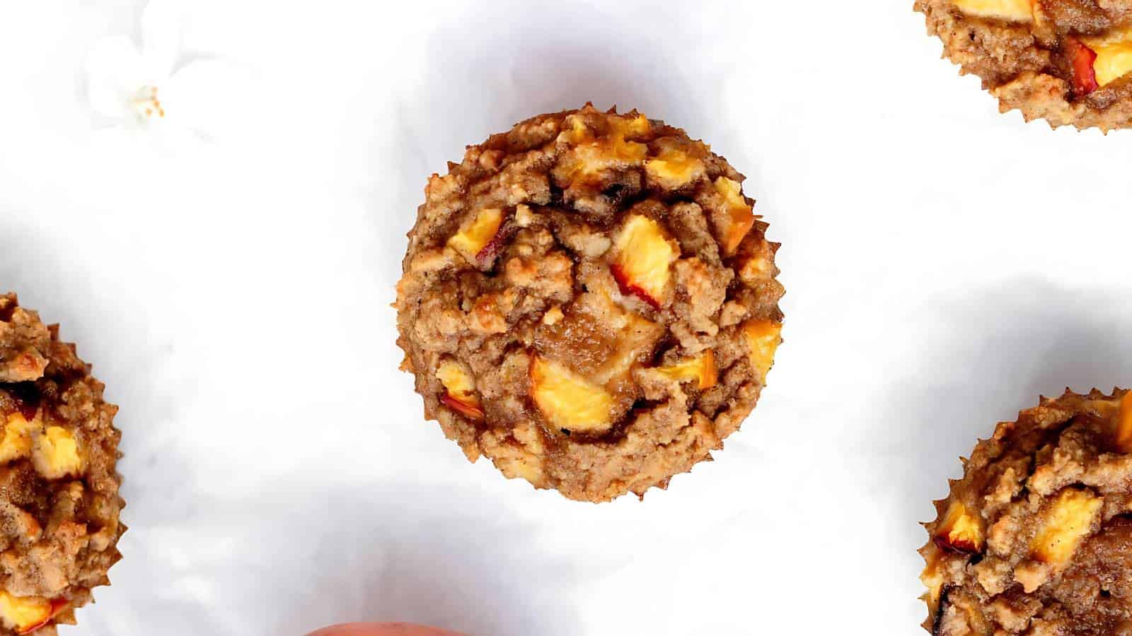 Top view of muffins with visible pieces of fruit and crumb topping on a white surface.