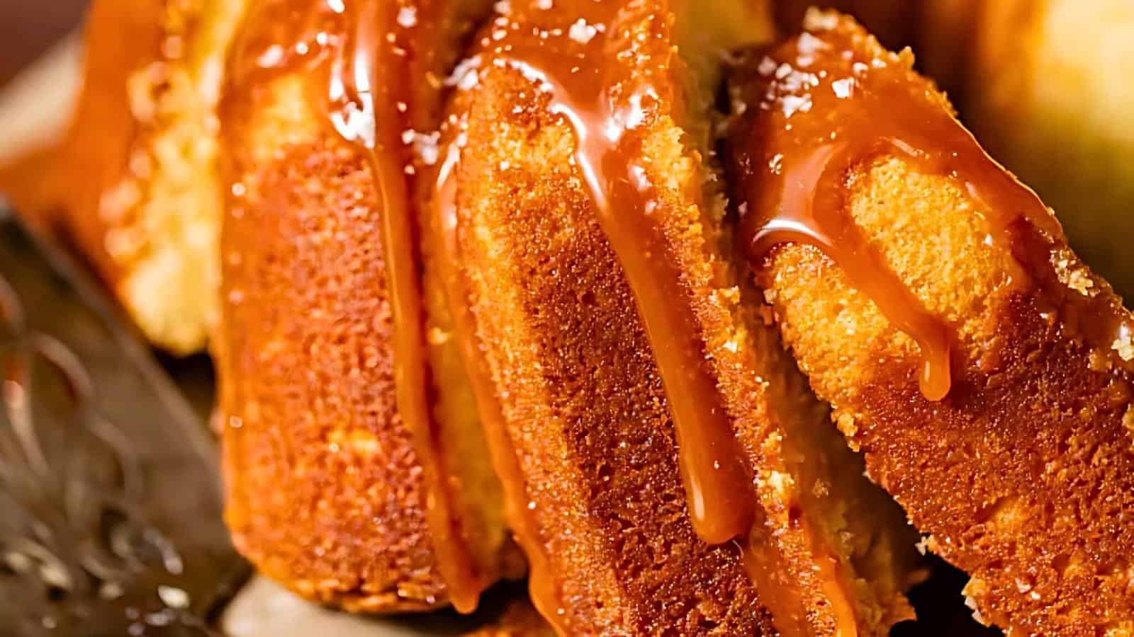 Close-up of a few thick slices of golden-brown cake drizzled with a glossy caramel sauce. The cake appears moist and tender, with the caramel adding a rich, smooth texture and a sweet touch to the dessert.