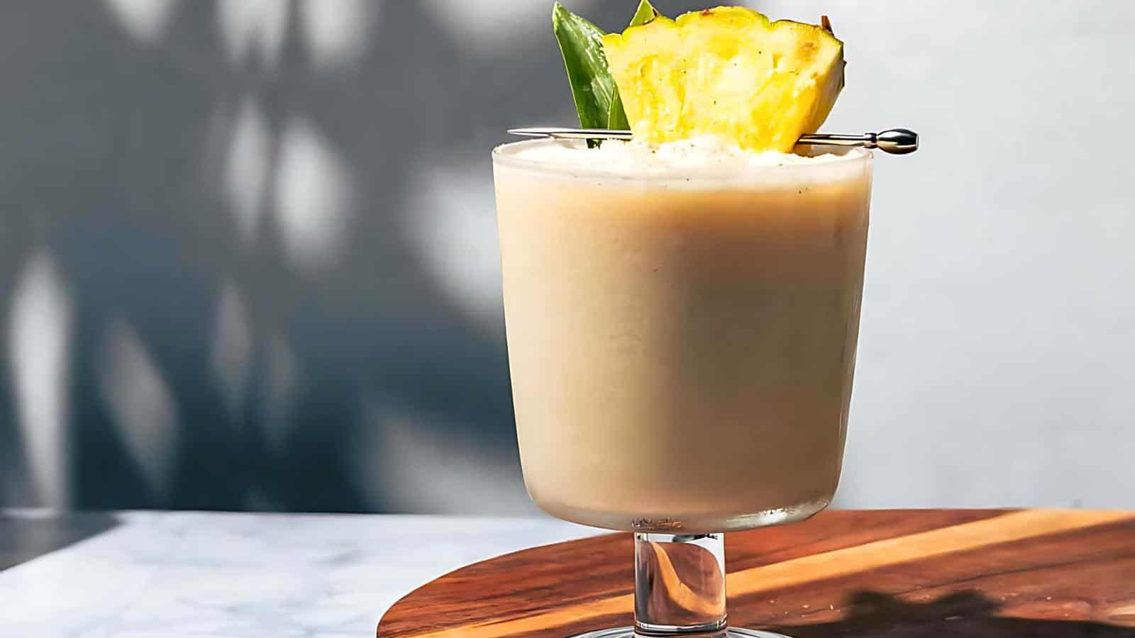 A drink garnished with a pineapple wedge and leaves, served in a clear glass on a wooden surface.