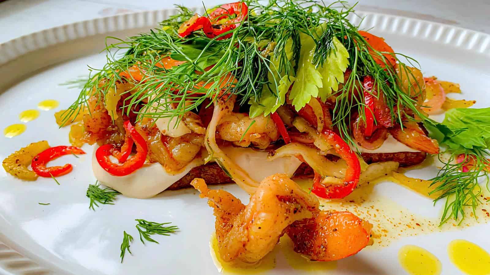 A pickled topped with shrimp, sliced peppers, greens, and cream sauce on a white plate.