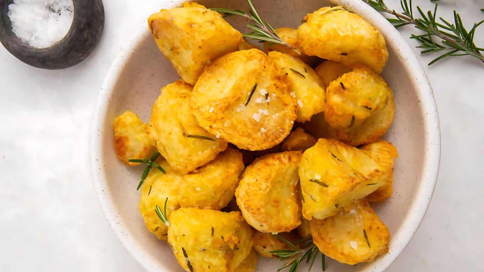 A bowl of golden roasted potatoes garnished with rosemary sprigs.